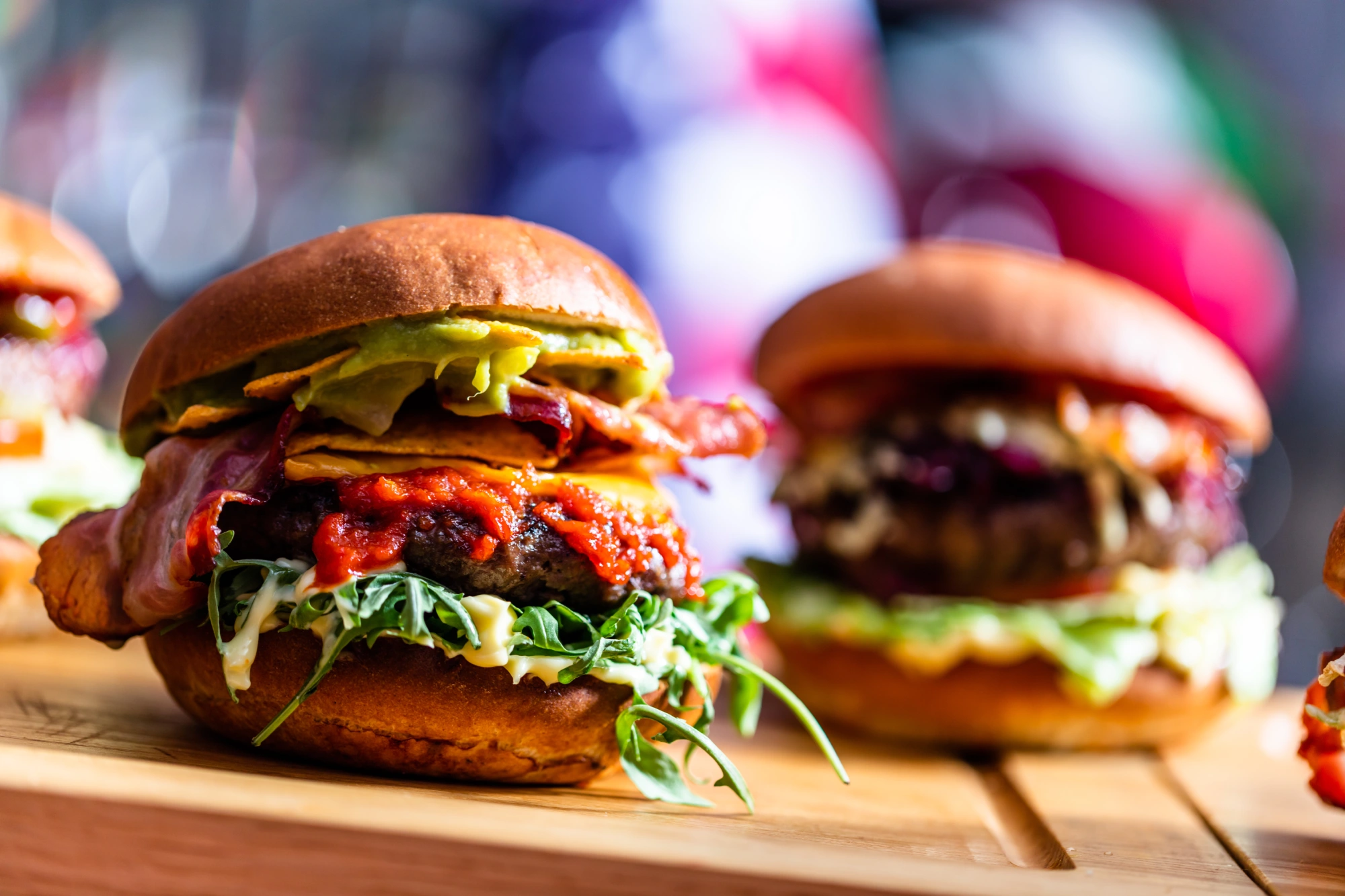 Gourmet burgers with toppings on wooden board.