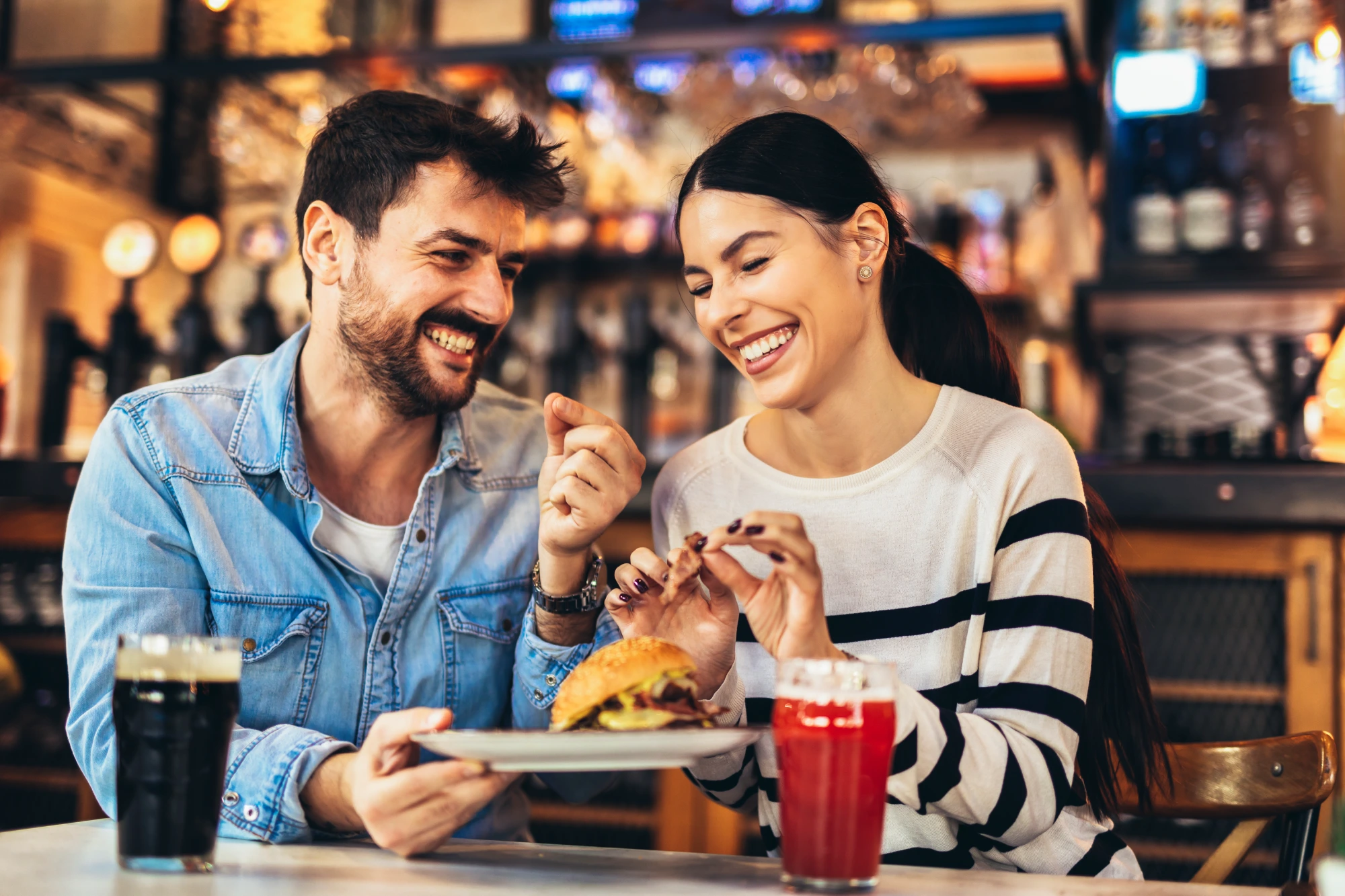 Couple enjoying burgers and drinks at bar.