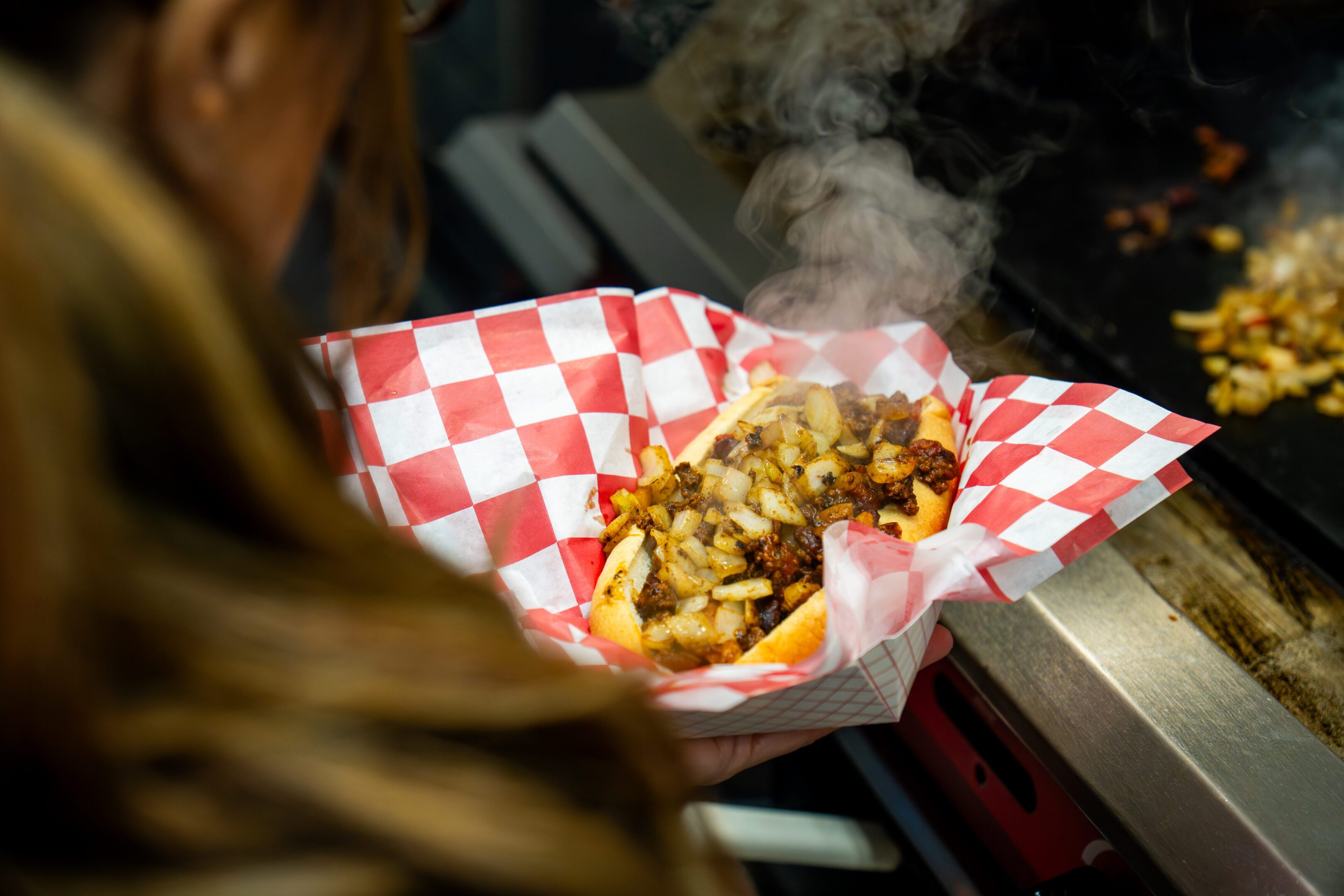 Steaming hot food served in a red and white checkered paper basket.