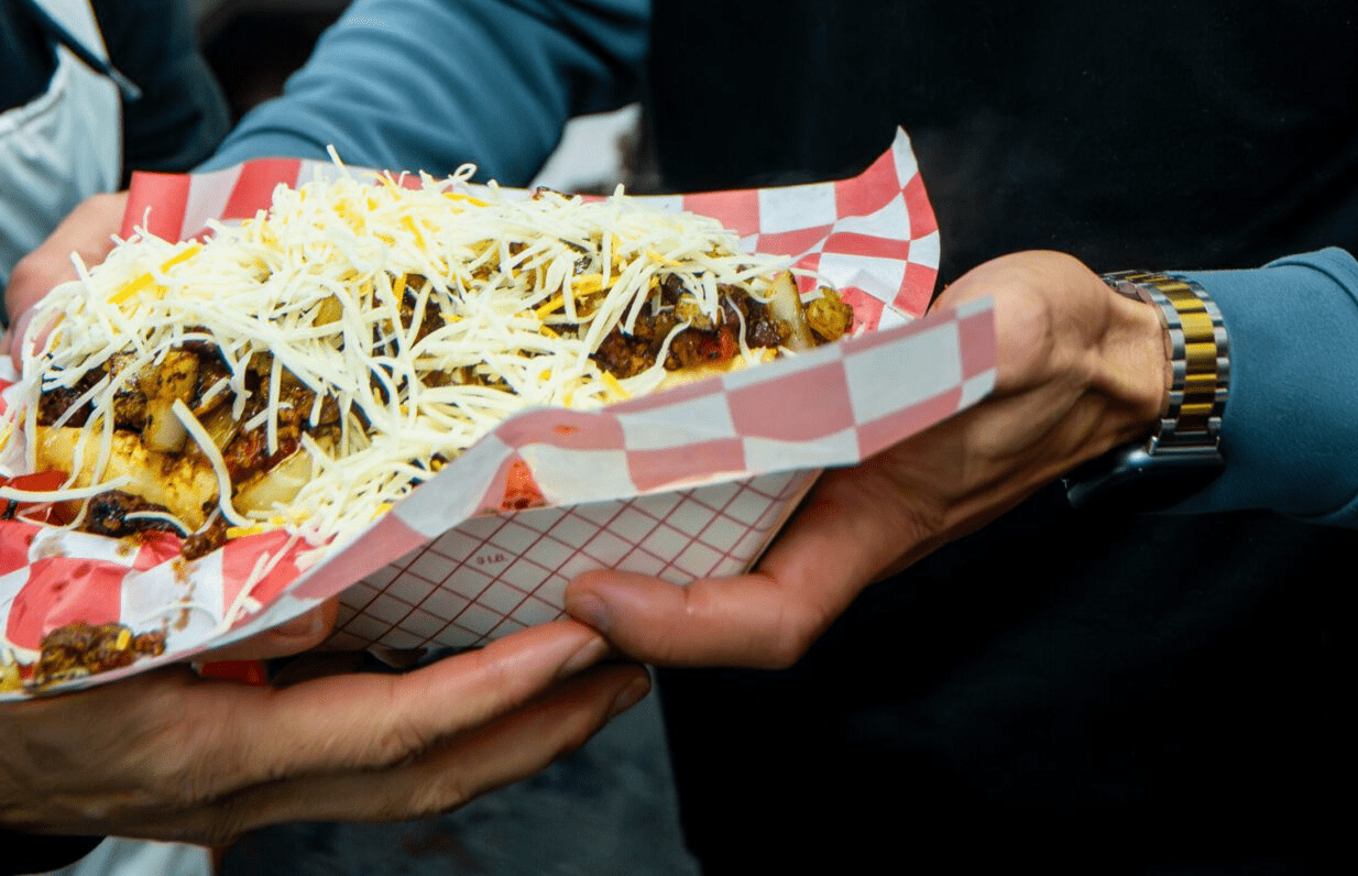 Person holding a loaded hot dog topped with shredded cheese.
