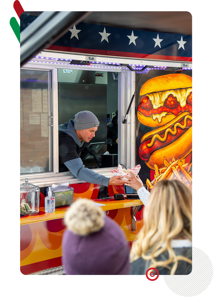 A vendor serving food from a colorful food truck to customers.