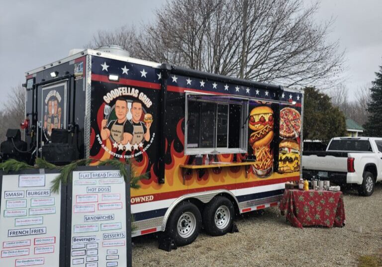 Food truck with fiery design serving barbecue dishes outdoors.